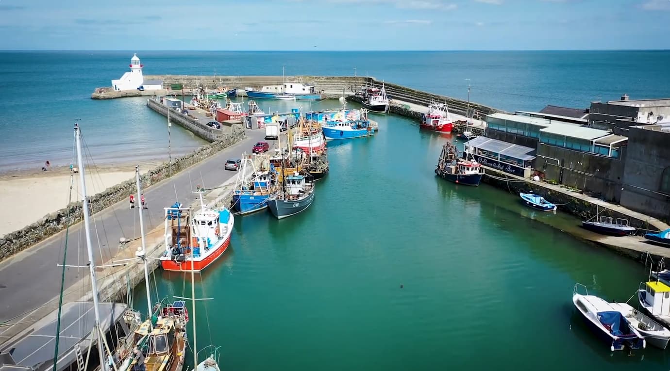 The bustling Balbriggan Harbour (1760s) with fishing boats moored and the iconic lighthouse in the background.